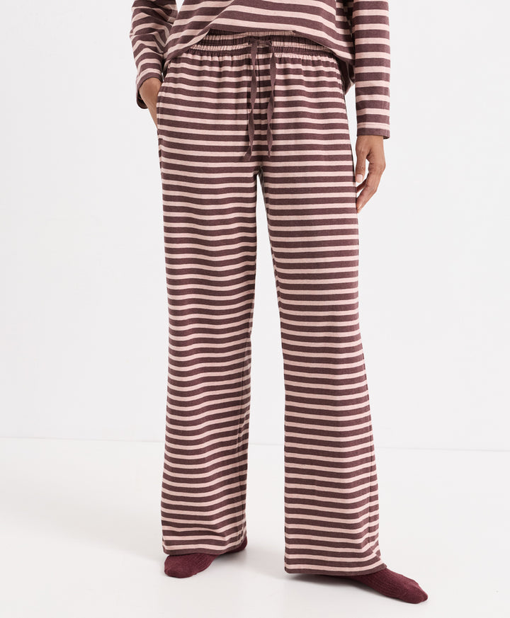 A person wearing loose, wide-leg striped lounge pants with a drawstring waist, paired with a matching striped long-sleeve top and burgundy socks, photographed against a clean white studio background.