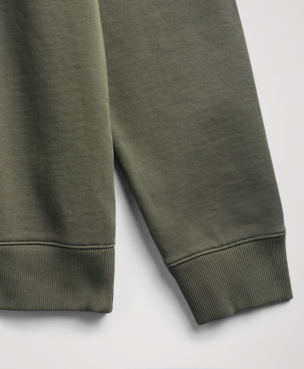 Close-up of a dusted green sweatshirt sleeve showing the ribbed cuff and textured fabric against a light gray background.
