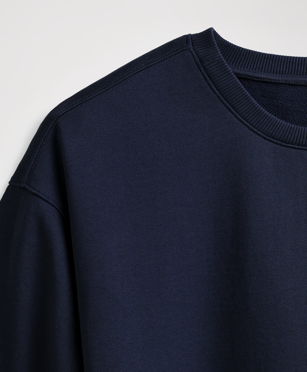 Close-up of a dark navy crewneck sweatshirt showing the ribbed collar and shoulder seam against a light gray background.