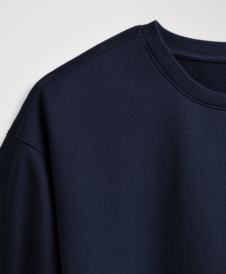 Close-up of a dark navy crewneck sweatshirt showing the ribbed collar and shoulder seam against a light gray background.