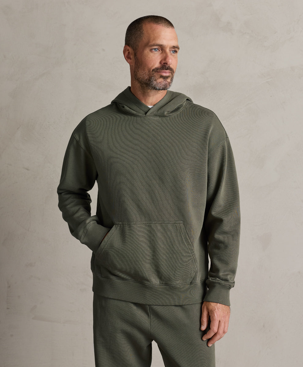 A man wearing a pact dusted green textured hoodie and matching sweatpants, standing against a neutral textured gray wall.