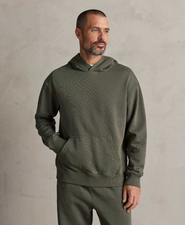 A man wearing a pact dusted green textured hoodie and matching sweatpants, standing against a neutral textured gray wall.