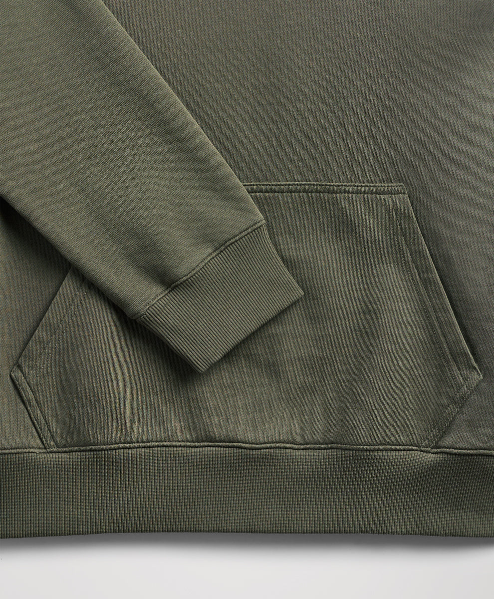 Close-up of a dusted green sweatshirt showing the sleeve cuff, ribbed hem, and a front kangaroo pocket.