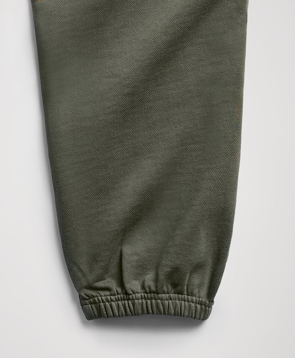Close-up of an dusted green fabric pant leg with an elasticized cuff, shown against a light gray background.
