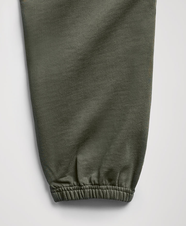 Close-up of an dusted green fabric pant leg with an elasticized cuff, shown against a light gray background.