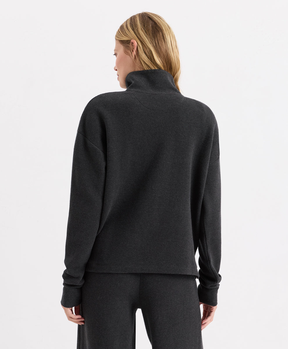 A woman shown from the back wearing a dark charcoal heather henley and matching dark gray pants against a clean white studio background.