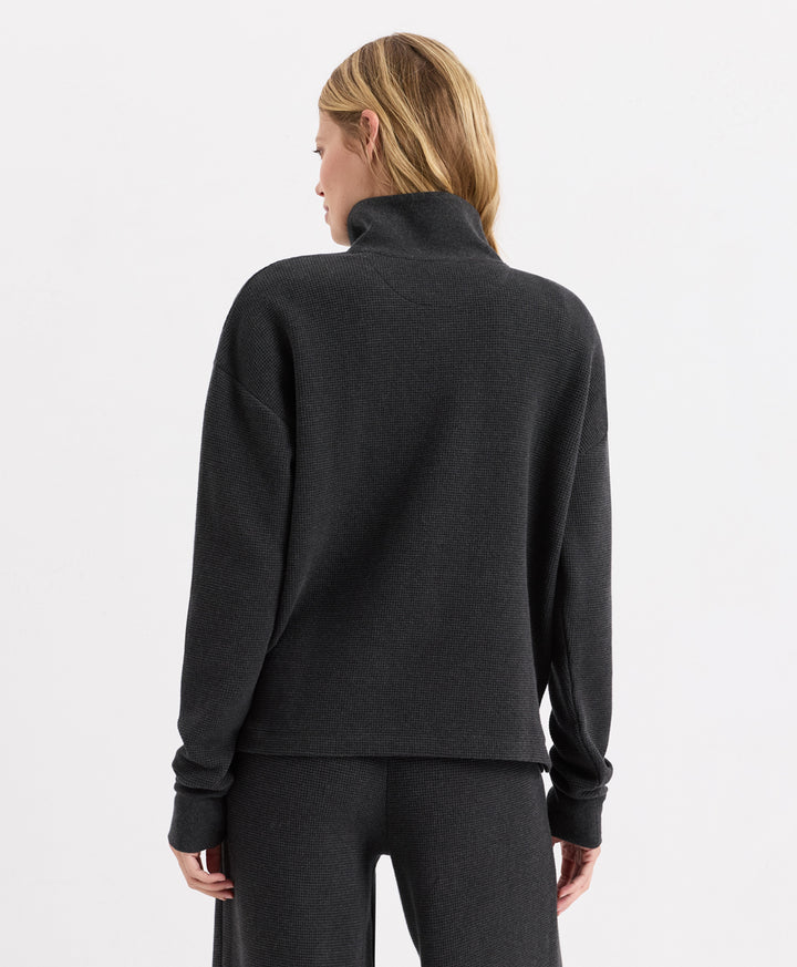 A woman shown from the back wearing a dark charcoal heather henley and matching dark gray pants against a clean white studio background.