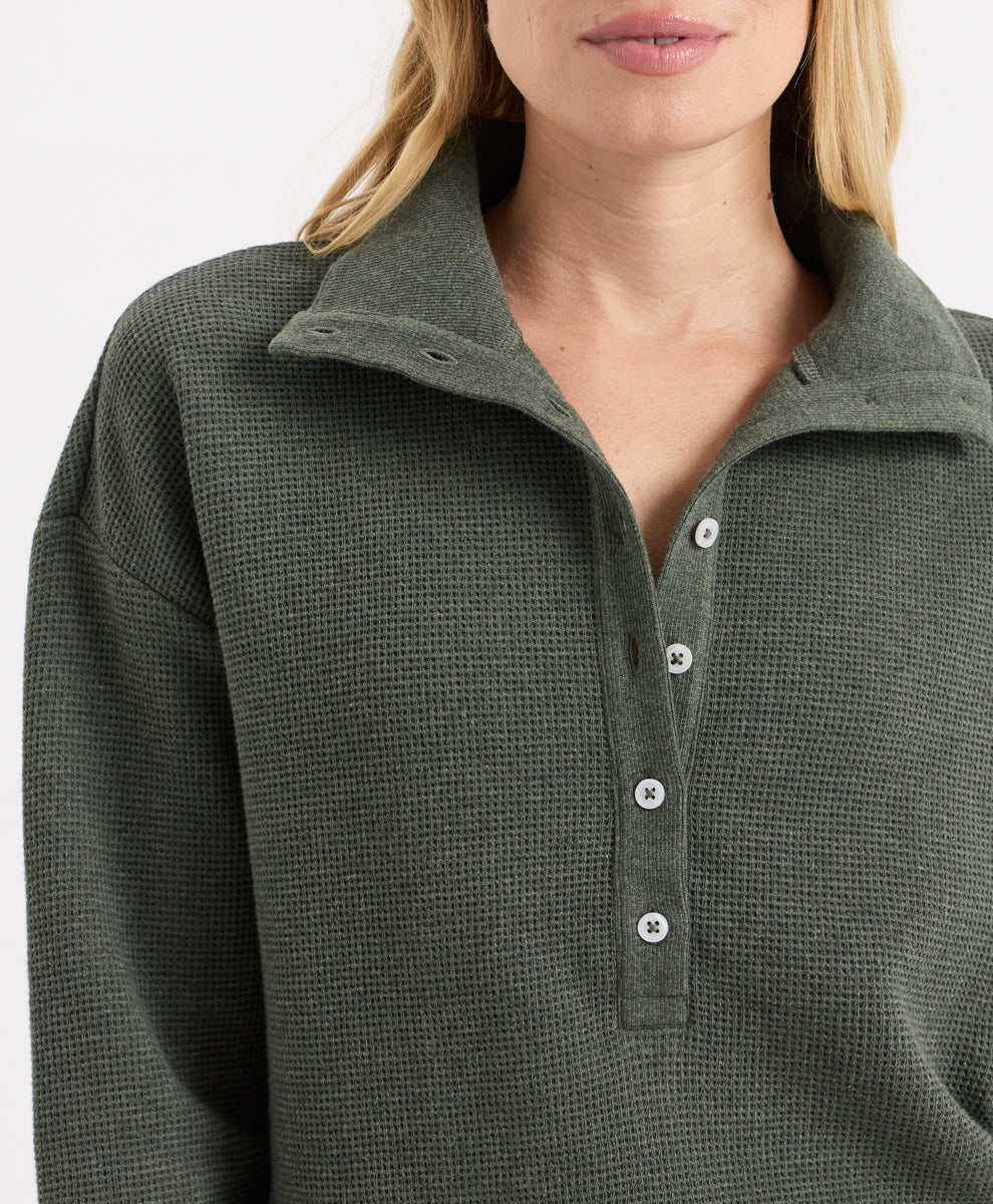 Close-up of a woman wearing a dusted green heather waffle-knit long-sleeve henley with white buttons.