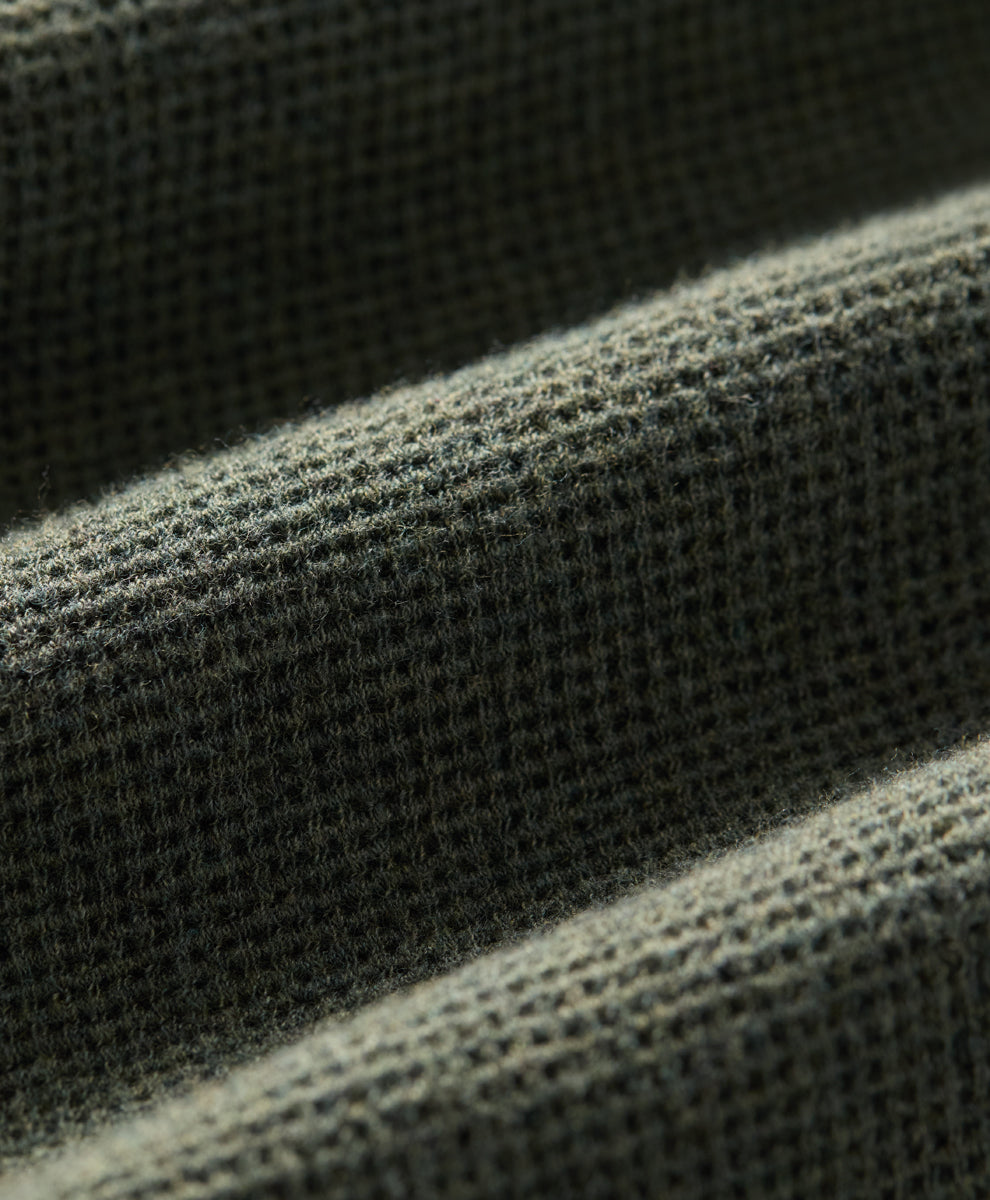 Close-up of a dusted green heather waffle-knit fabric texture with soft diagonal folds.