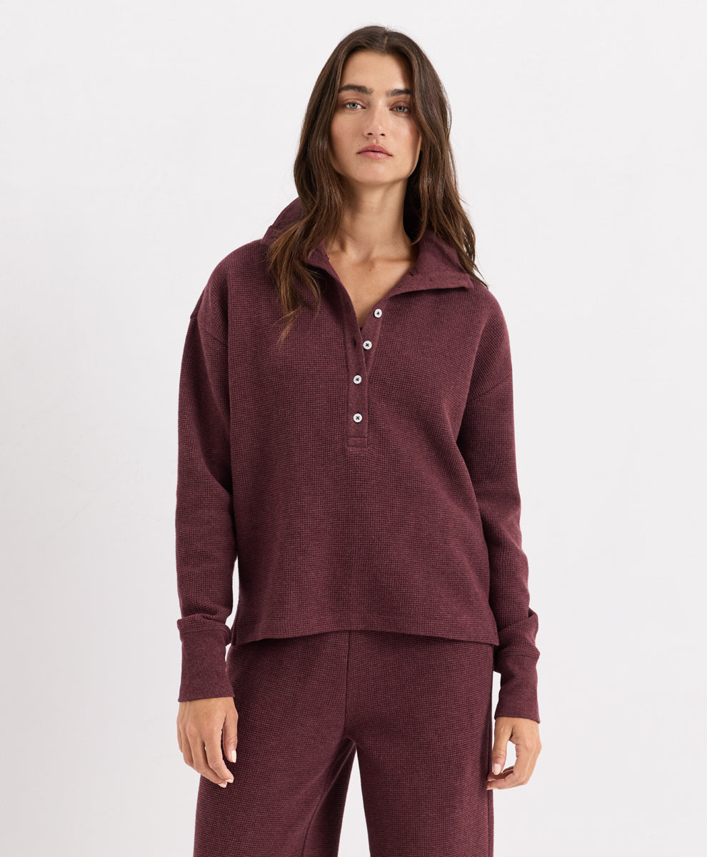 A woman modeling a matching merlot heather knit loungewear set, featuring a long-sleeve henley and matching pants, shot against a plain white studio background.
