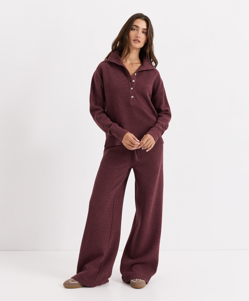A woman modeling a matching two-piece loungewear set in merlot heather, featuring a long-sleeve half-button henley top and wide-leg pants, against a plain white studio background.