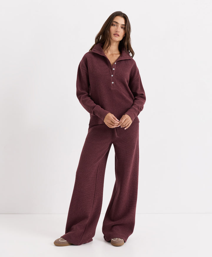 A woman modeling a matching two-piece loungewear set in merlot heather, featuring a long-sleeve half-button henley top and wide-leg pants, against a plain white studio background.