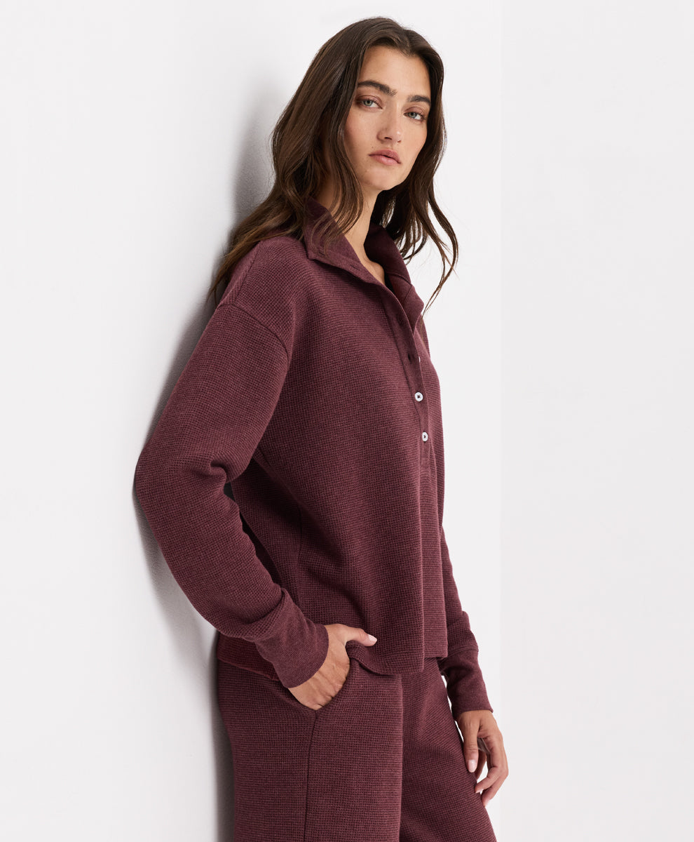 A woman wearing a matching merlot heather knit lounge set, featuring a long-sleeve henley and coordinating pants, posed against a clean white wall.