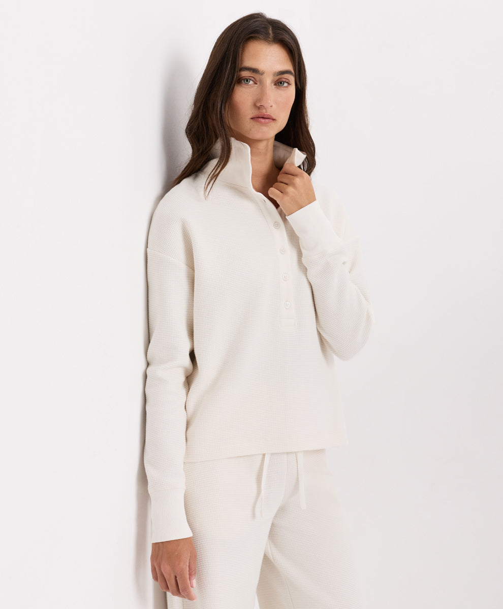 A woman modeling a soft ivory knit henley with matching drawstring pants against a plain white studio background.