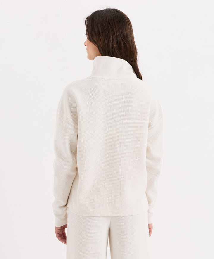 A woman shown from the back wearing a soft ivory henley with matching pants, against a plain white studio background.