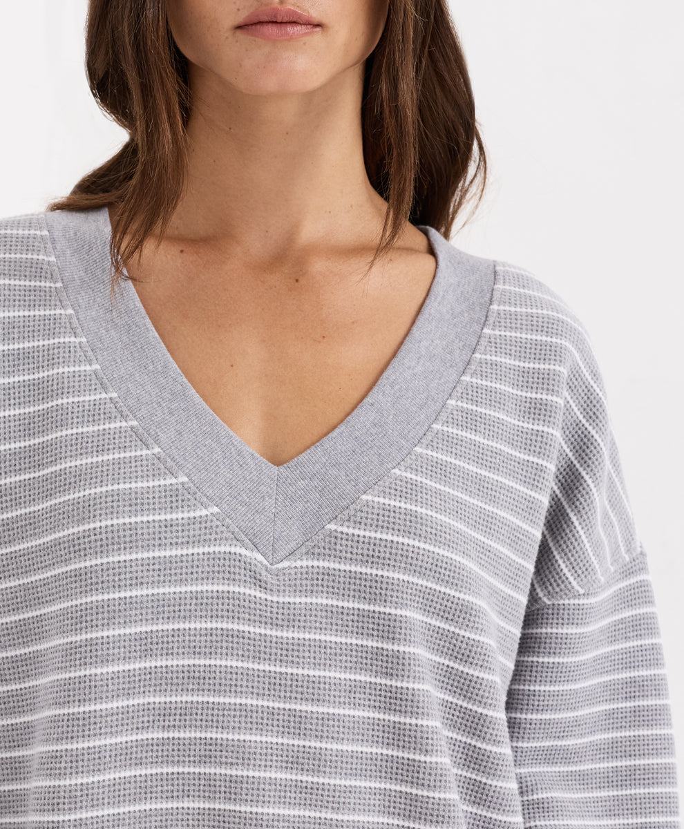 Close-up of a woman wearing a gray and white horizontally striped waffle-knit V-neck top.