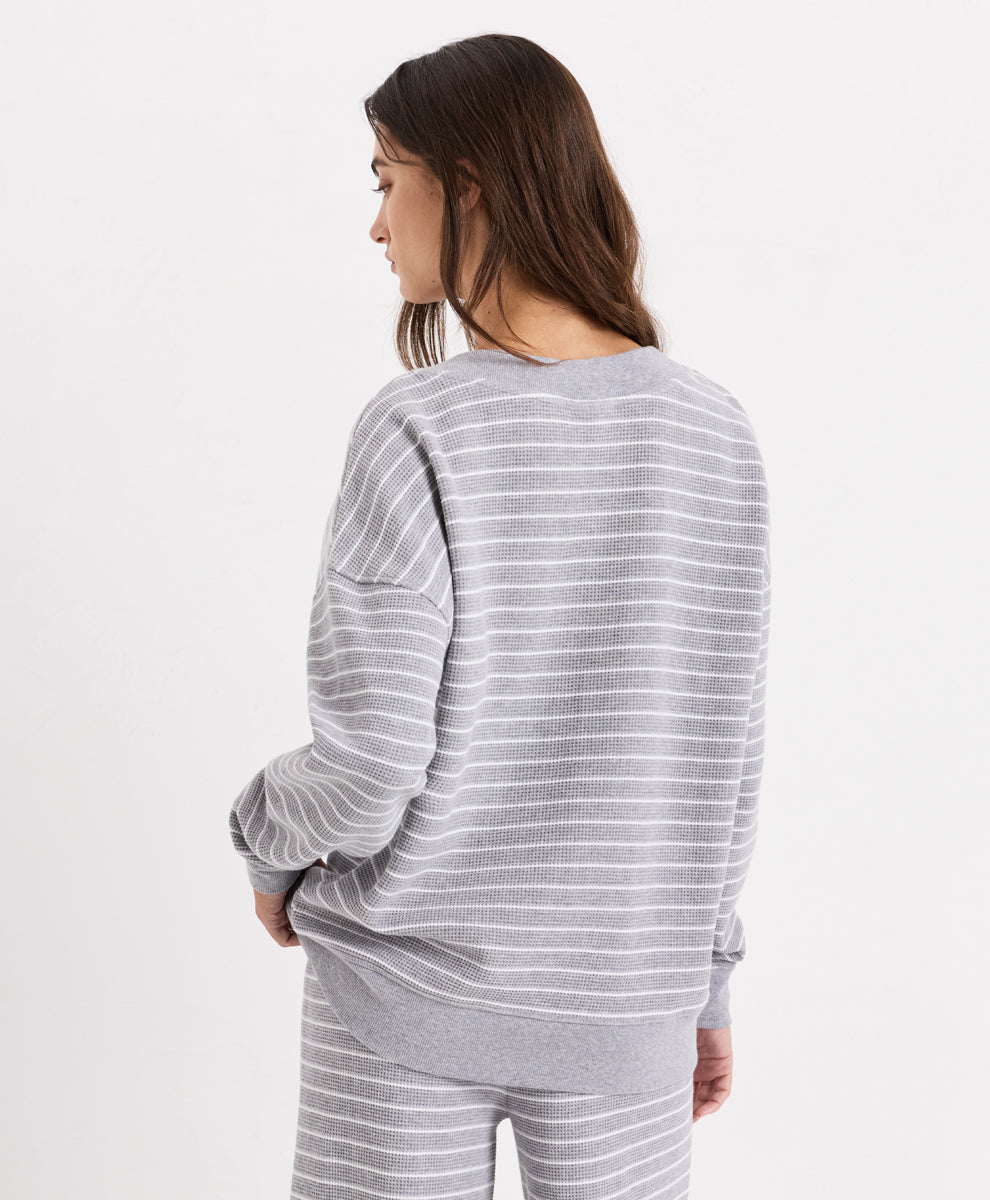 A woman shown from the back wearing a light gray and white horizontally striped V-neck top and matching striped pants against a plain white studio background.