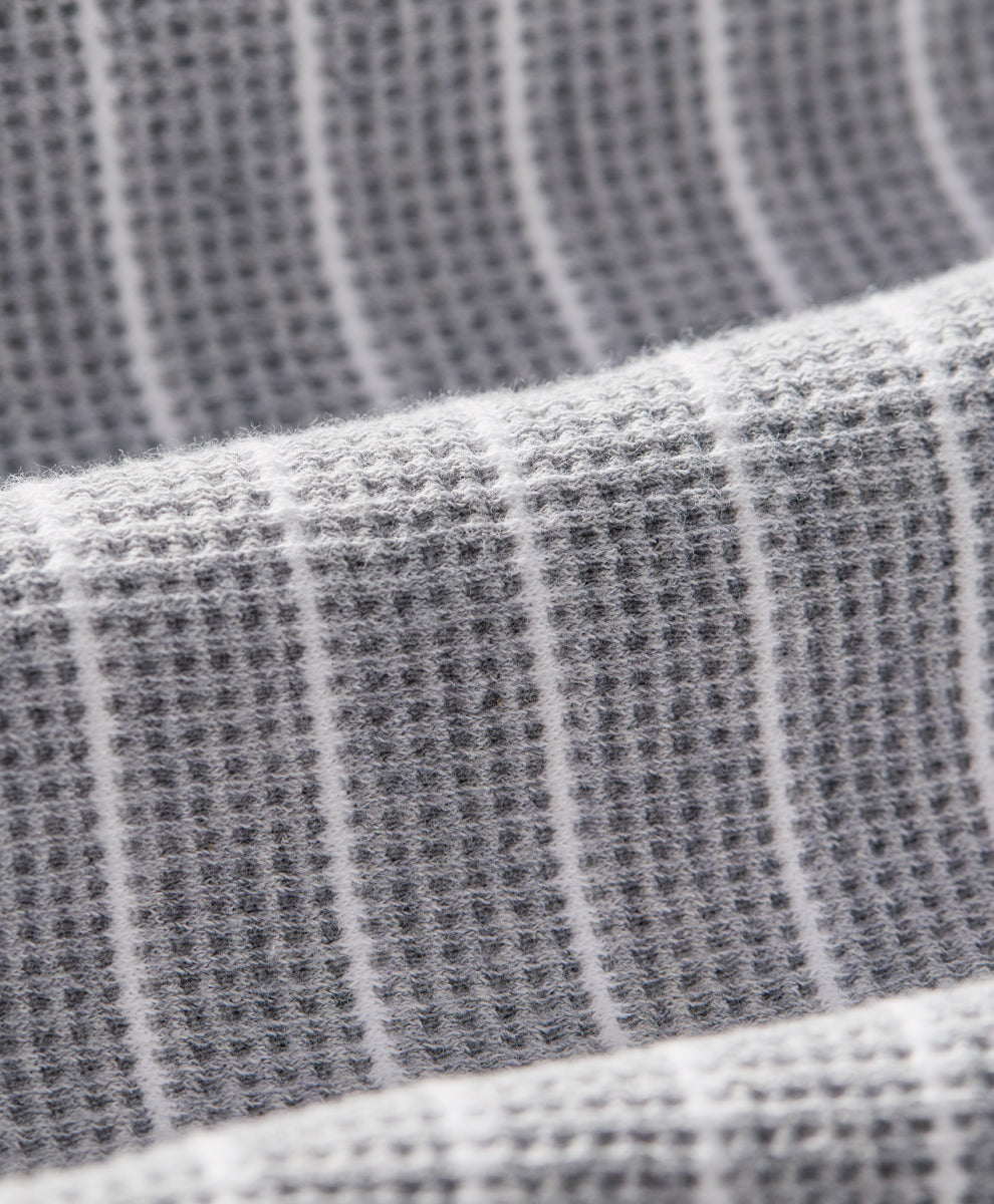 Close-up of a gray waffle-weave fabric with thin white vertical stripes, showing the textured weave and soft folds.