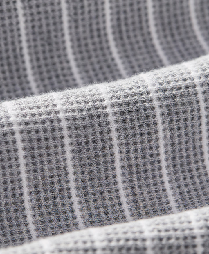 Close-up of a gray waffle-weave fabric with thin white vertical stripes, showing the textured weave and soft folds.