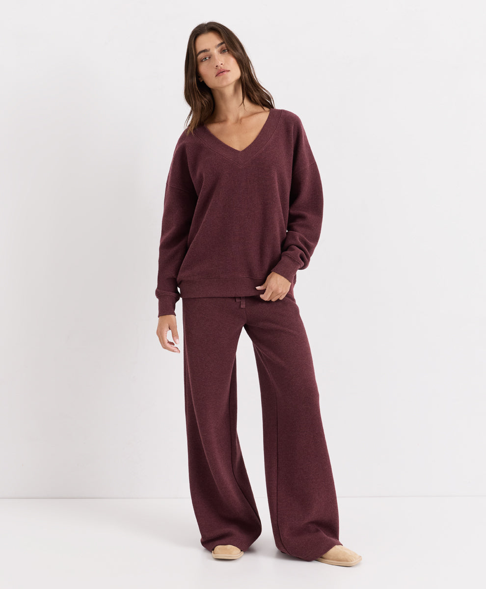 A woman modeling a matching merlot heather waffle loungewear set consisting of a V-neck long-sleeve top and wide-leg pants, photographed against a clean white studio background.
