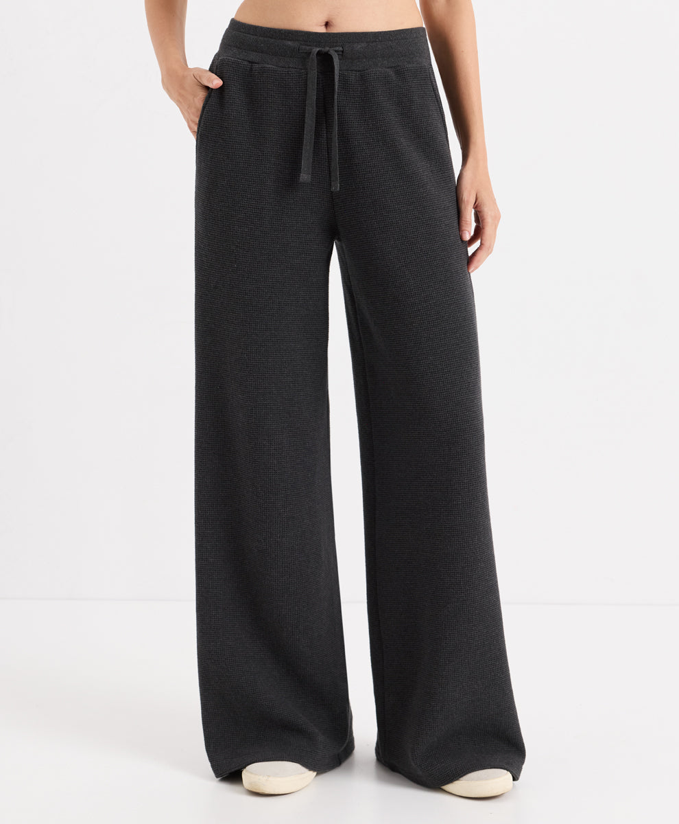 A person wearing dark charcoal heather wide-leg pants with a drawstring waistband, shown from the waist down against a clean white studio background.