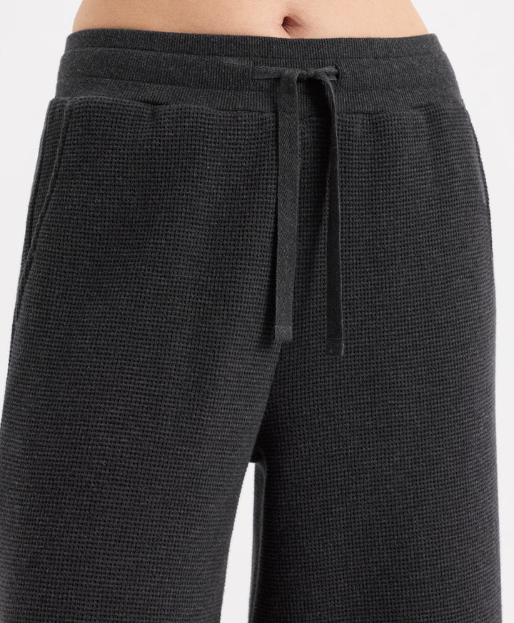 Close-up of a person wearing dark charcoal heather textured lounge pants with a matching drawstring waistband, shown against a light gray studio background.