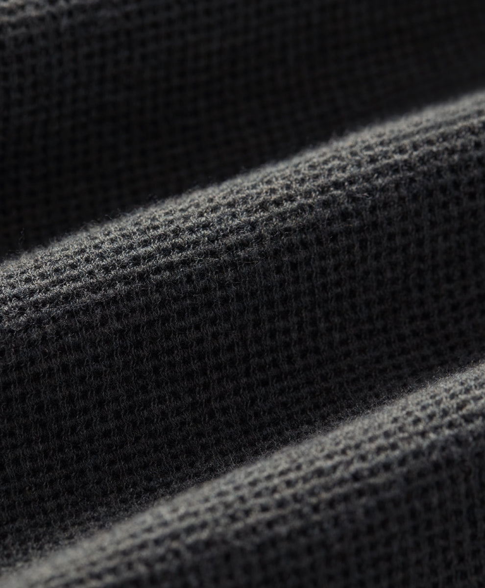 Close-up of a dark charcoal heather waffle-knit fabric texture with soft diagonal folds.