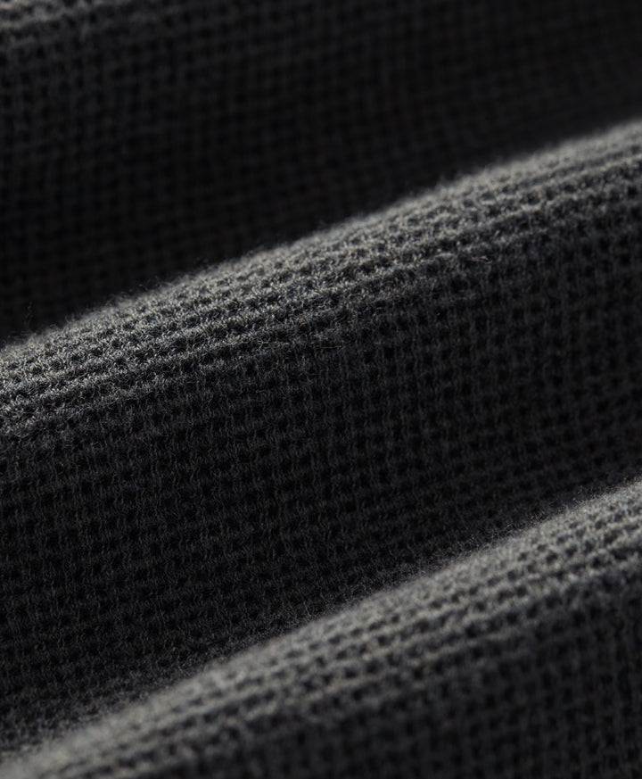 Close-up of a dark charcoal heather waffle-knit fabric texture with soft diagonal folds.