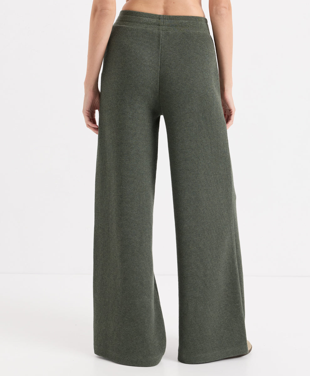 A model shown from the back wearing dusted green heather wide-leg knit pants against a clean white studio background.