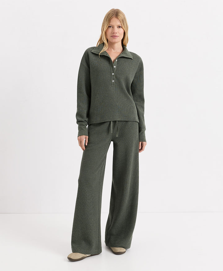 A woman modeling a matching two-piece knit loungewear set in dusted green heather, featuring a long-sleeve henley top with a button placket and matching wide-leg pants, against a plain white studio background.