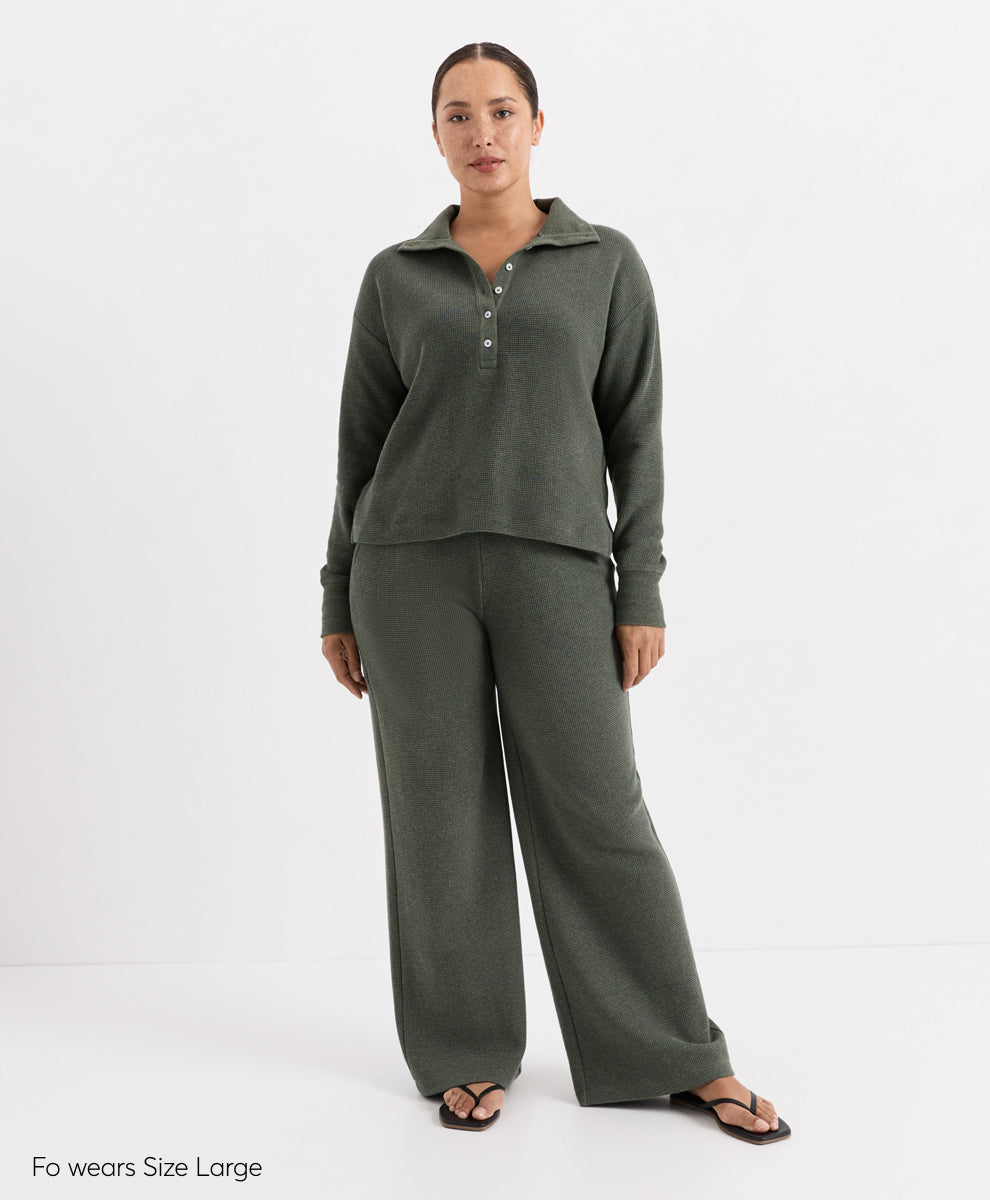 A woman modeling a matching two-piece lounge set in dusted green heather, featuring a long-sleeve henley top with a button placket and wide-leg pants, photographed against a plain white studio background.