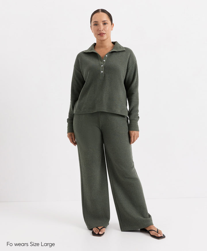 A woman modeling a matching two-piece lounge set in dusted green heather, featuring a long-sleeve henley top with a button placket and wide-leg pants, photographed against a plain white studio background.