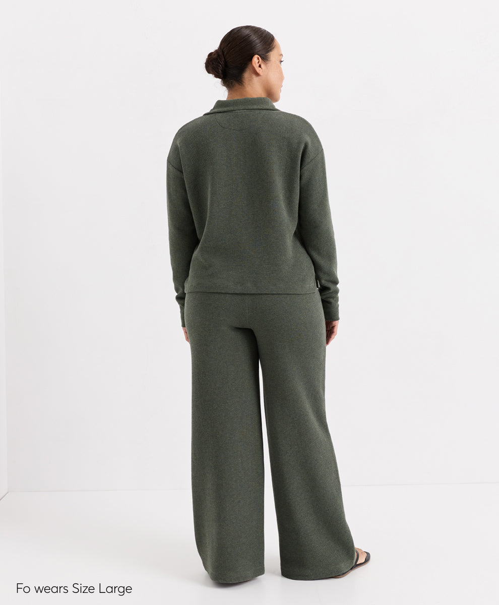 A woman shown from the back wearing a matching dusted green heatherknit lounge set consisting of a long-sleeve Henley top and wide-leg pants, photographed against a clean white studio background.