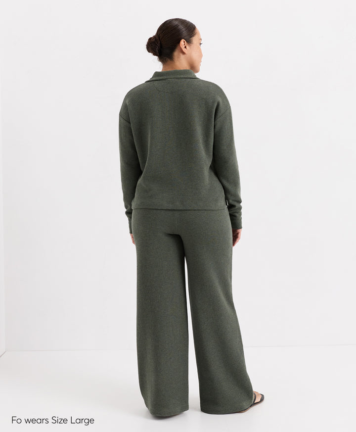 A woman shown from the back wearing a matching dusted green heatherknit lounge set consisting of a long-sleeve Henley top and wide-leg pants, photographed against a clean white studio background.