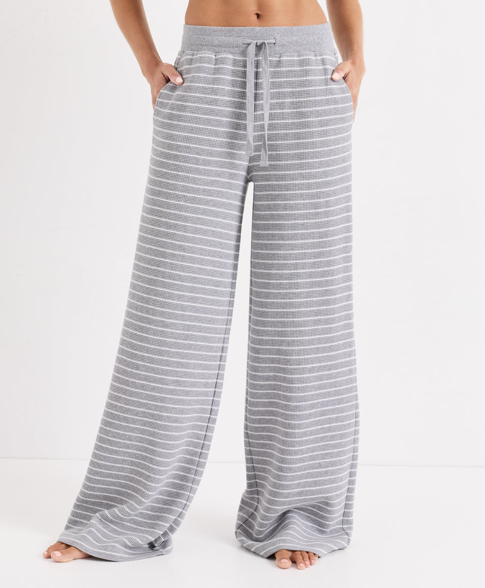 A person wearing gray wide-leg lounge pants with thin white horizontal stripes, shown from the waist down against a clean white studio background.