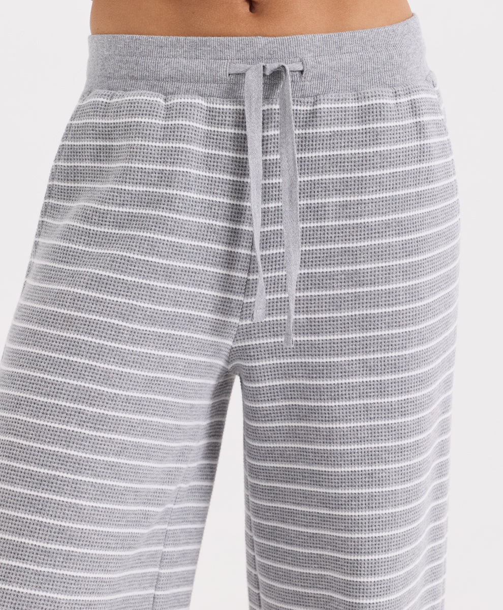 Close-up of a person wearing gray waffle-knit pants with thin white horizontal stripes and a matching gray drawstring waistband.