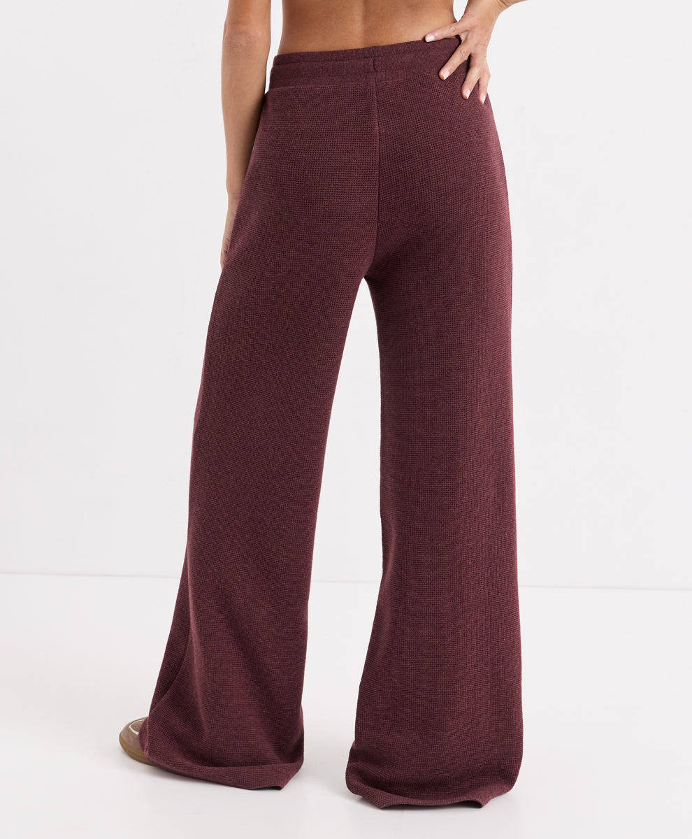 A person shown from the back wearing loose, wide-leg knit pants in merlot heather, photographed against a clean white studio background.