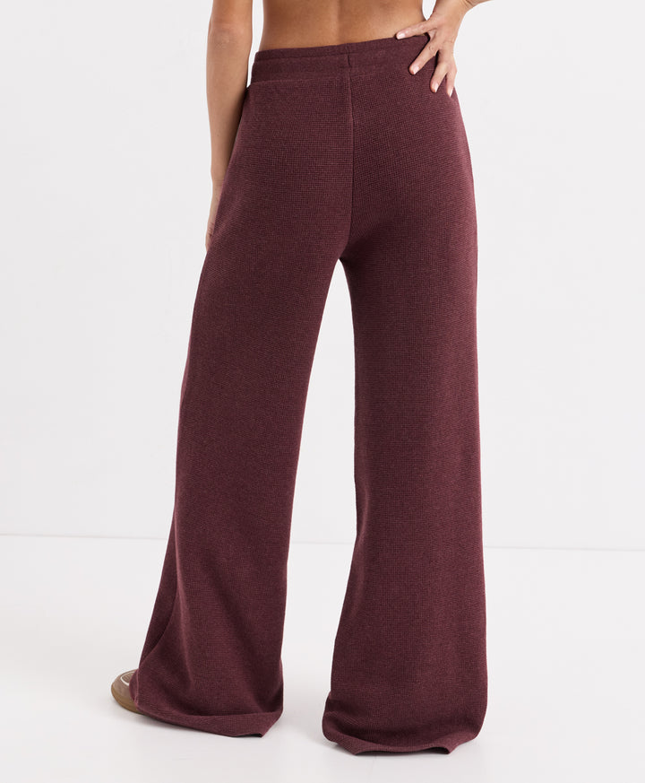A person shown from the back wearing loose, wide-leg knit pants in merlot heather, photographed against a clean white studio background.