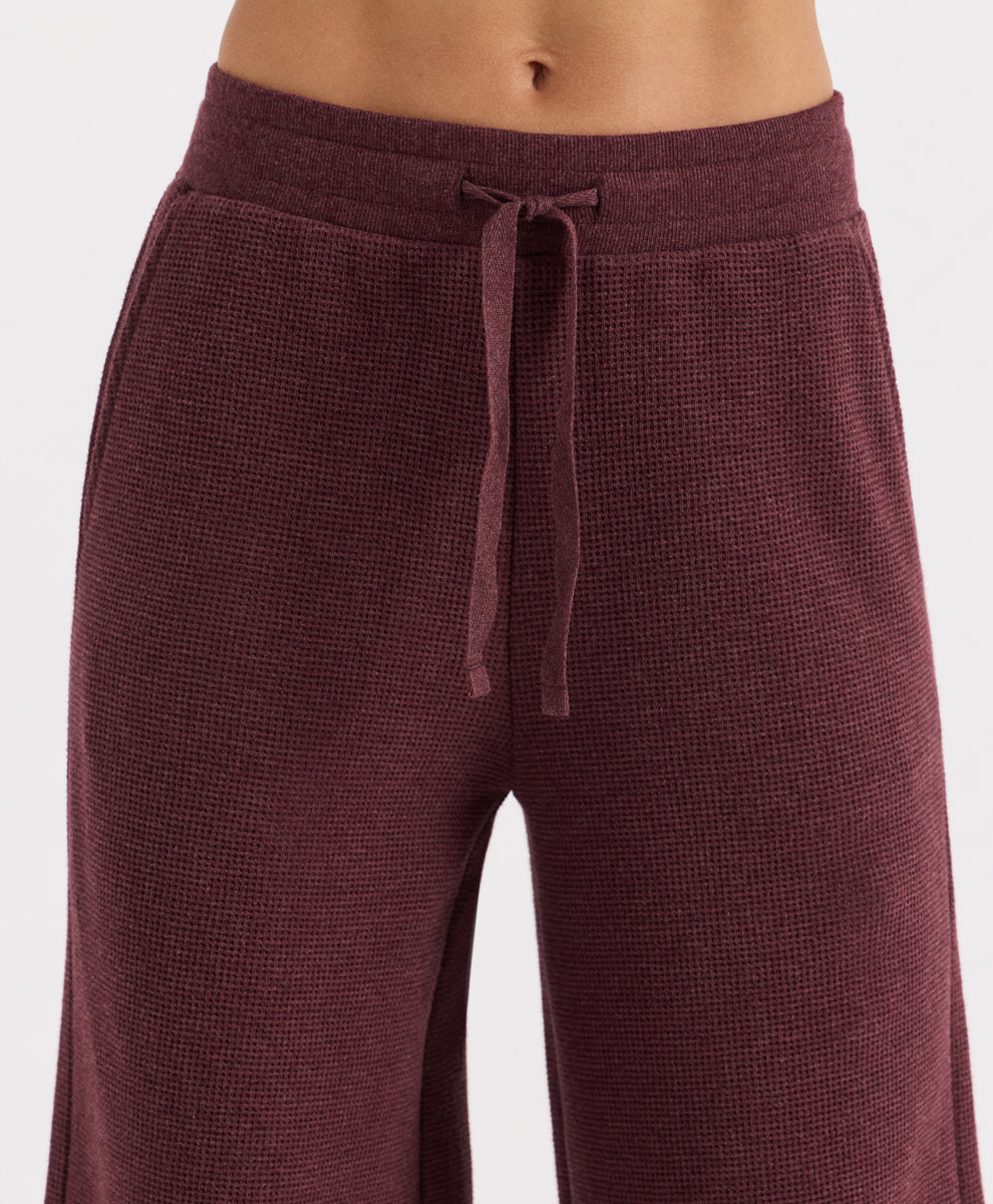 Close-up of a person wearing textured waffle-knit lounge pants in merlot heather, with a matching drawstring waistband, against a light gray studio background.