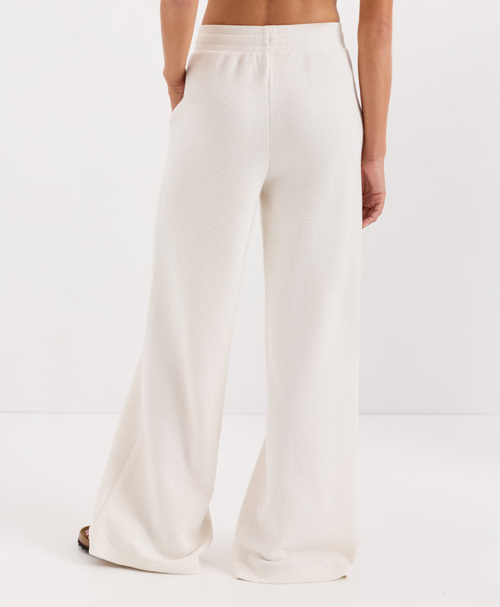 A model from the back wearing soft ivory wide-leg pants, shown against a clean white studio background.