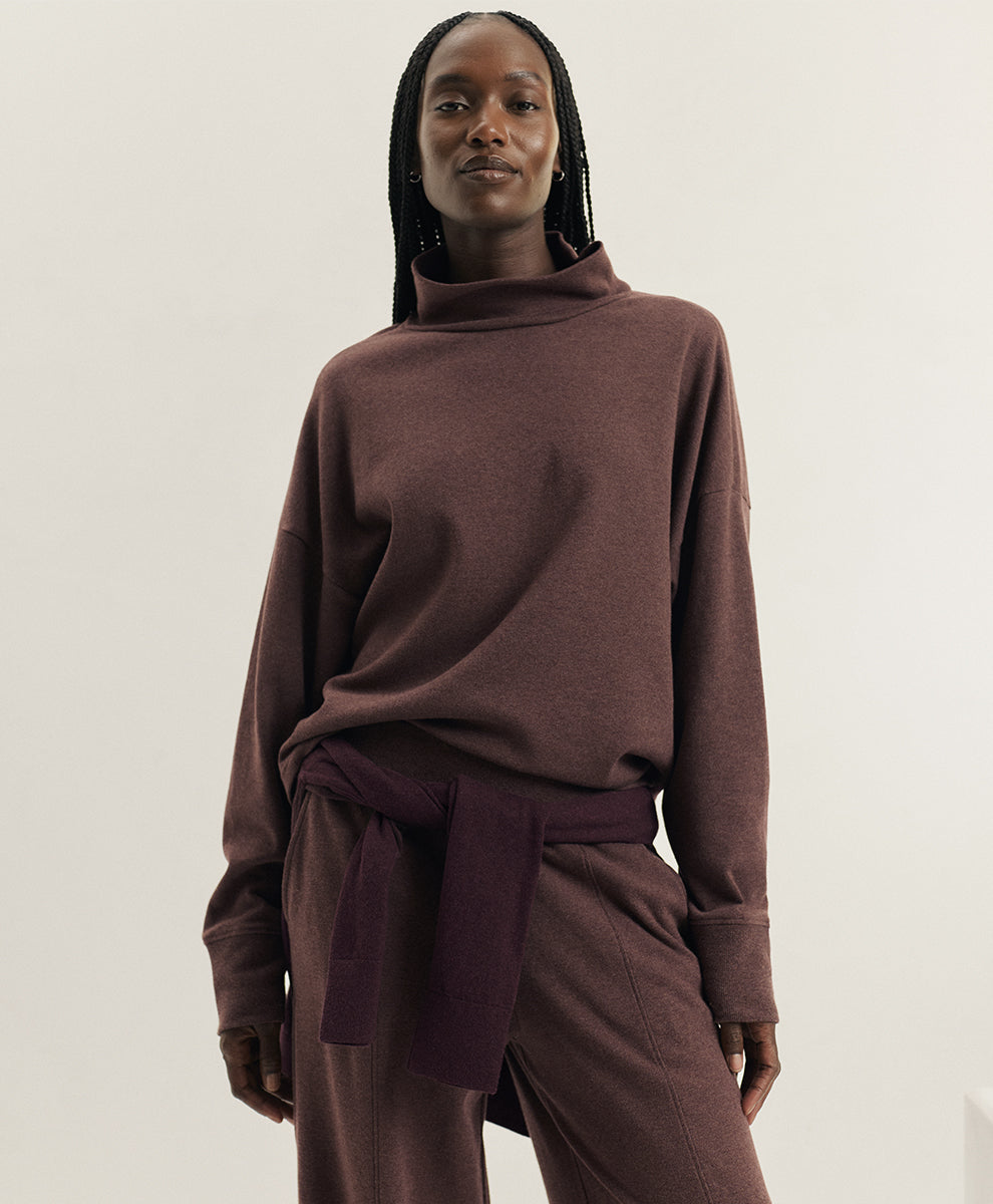 A model wearing a matching chestnut heather knit set consisting of a long-sleeve funnel-neck top and coordinating pants, against a plain off-white studio background.