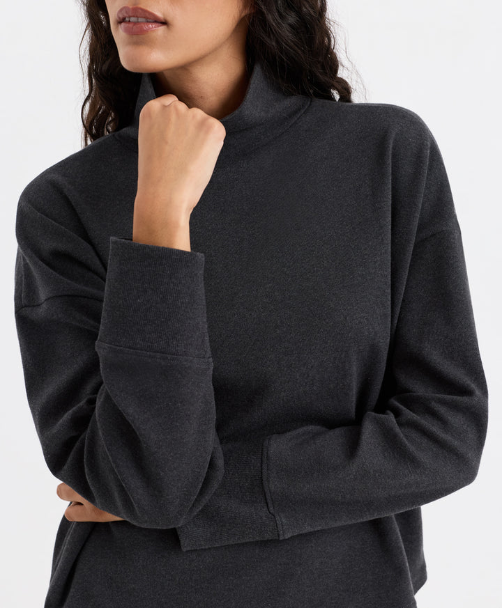 A close-up of a woman wearing a dark charcoal heather funnel neck top showing the texture of the fabric and the high collar.