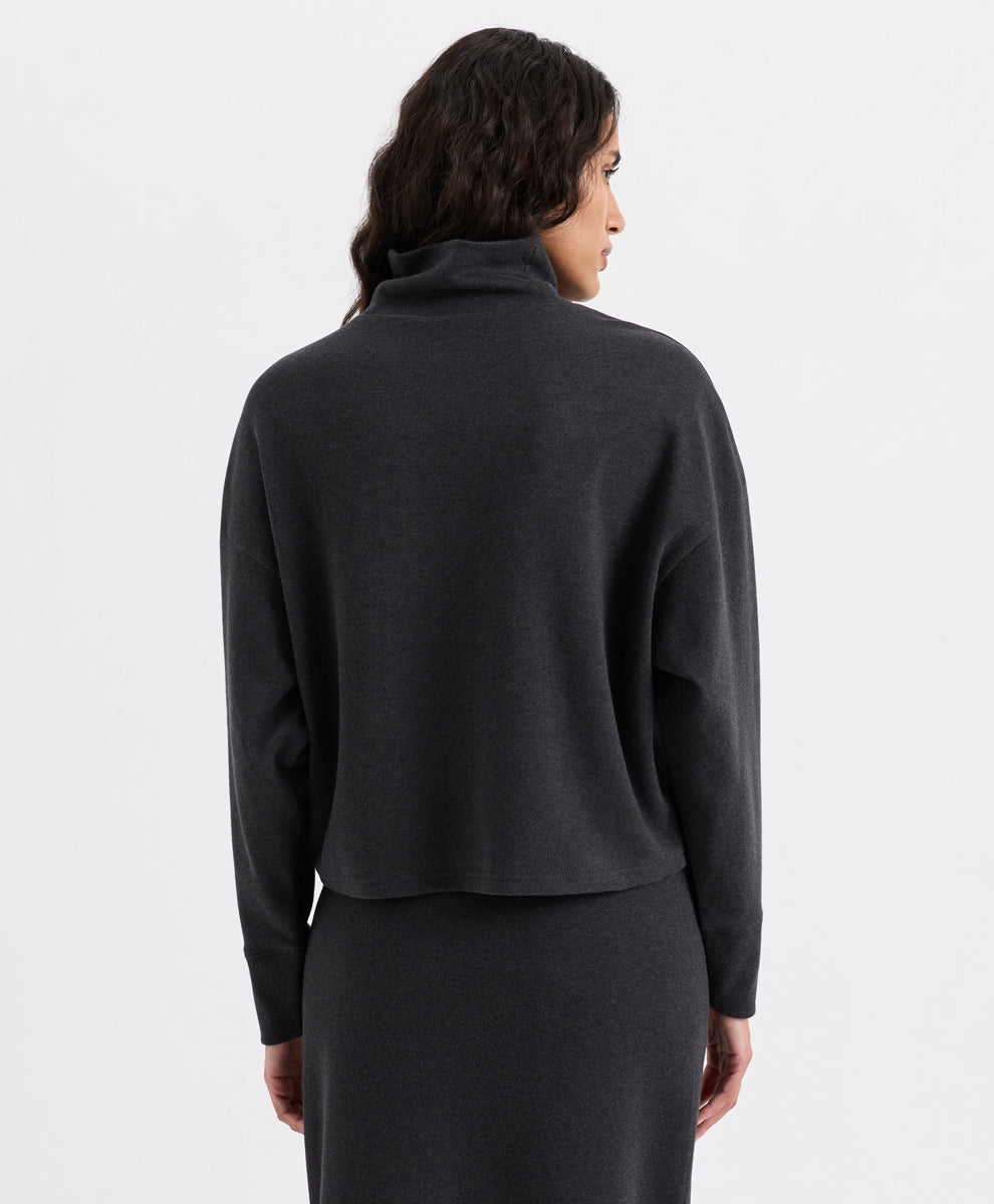 A woman shown from the back wearing a dark charcoal heather funnel neck top and a matching dark skirt against a plain light gray studio background.