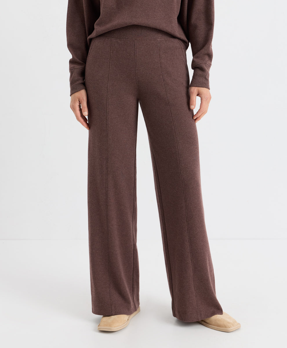 A model is shown from the waist down wearing a matching chestnut heather knit sweater and wide-leg trousers, paired with beige slip-on shoes, against a plain white studio background.