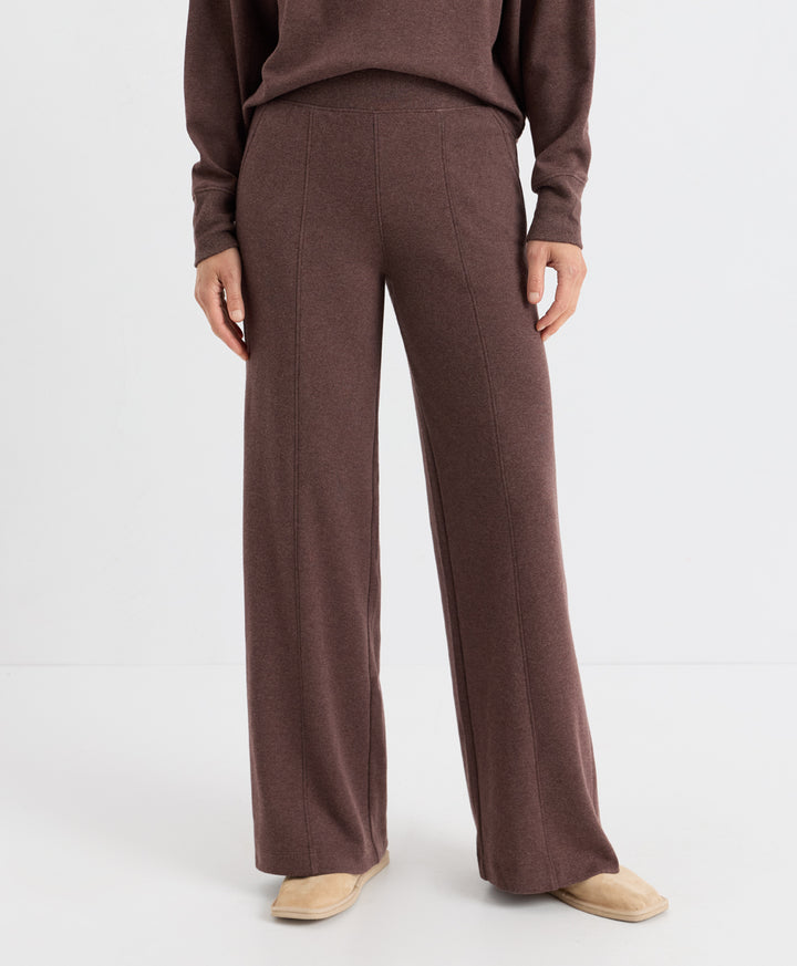 A model is shown from the waist down wearing a matching chestnut heather knit sweater and wide-leg trousers, paired with beige slip-on shoes, against a plain white studio background.