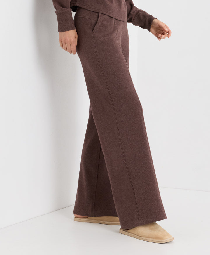 A person wearing a matching chestnut heather knit lounge set with wide-leg pants and a long-sleeve top, paired with beige slip-on slippers against a clean white studio background.