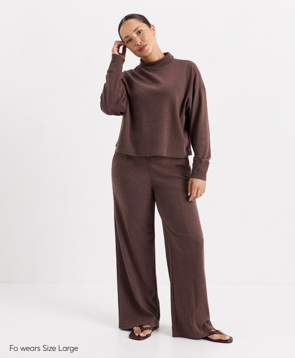A woman modeling a matching two-piece lounge set in cocoa, featuring a long-sleeve mock neck top and wide-leg pants, against a plain white studio background.