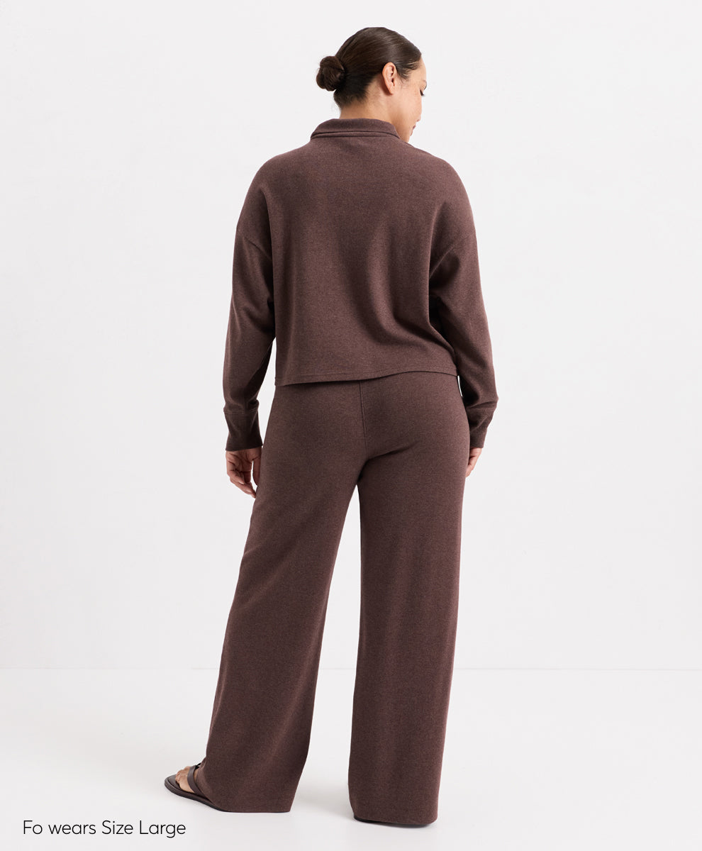 A model shown from the back wearing a matching chestnut heather knit lounge set consisting of a cropped quarter-zip long-sleeve top and wide-leg pants, on a white studio background.