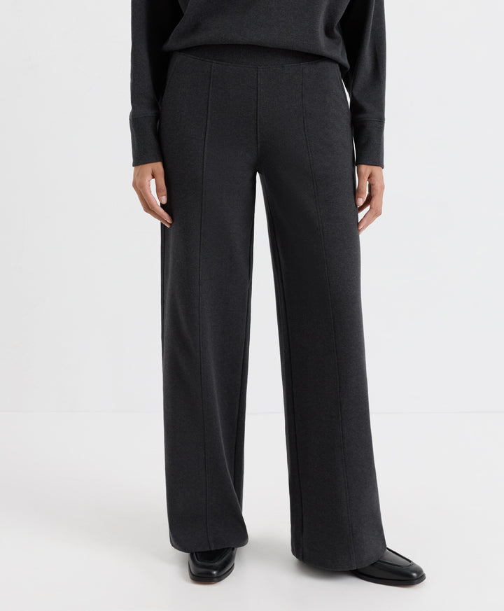 A model wearing dark charcoal heather wide-leg trousers, a matching long-sleeve top, and black leather shoes, shown from the waist down against a plain white studio background.