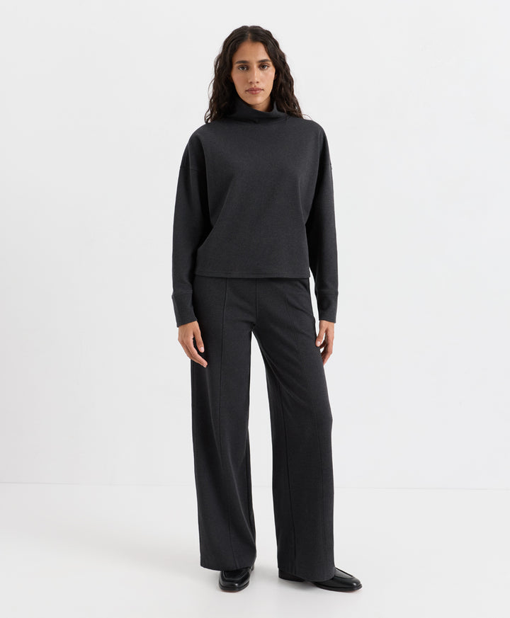 A woman modeling a dark charcoal heather knit two-piece set consisting of a long-sleeve mock-neck top and matching wide-leg trousers, photographed against a seamless white studio background.